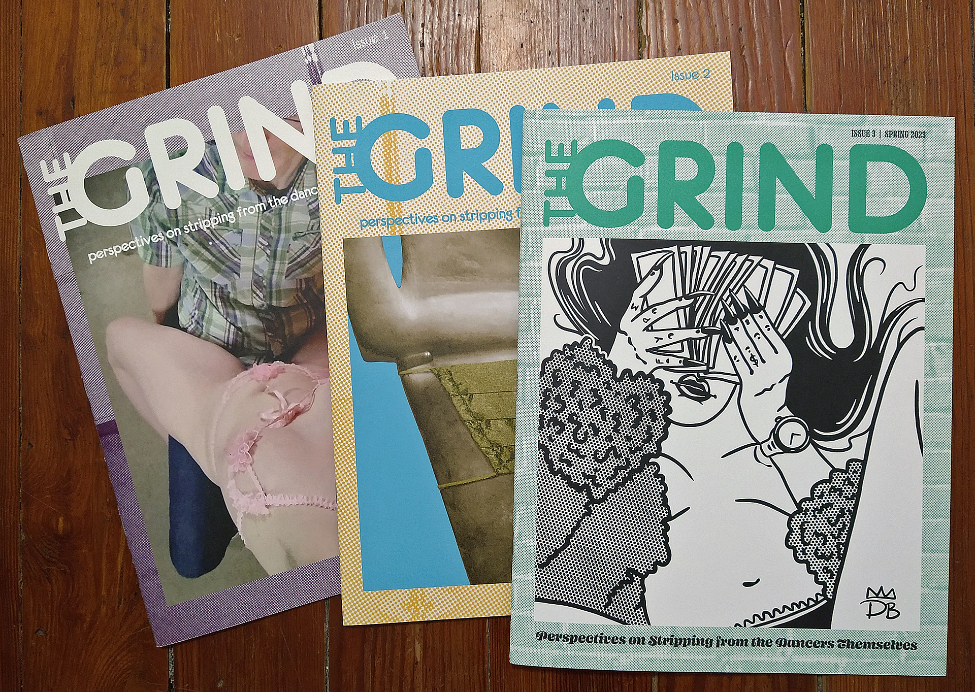 3 different issues of The GRIND magazine are displayed from earliest to latest, fanned out on a wooden background.